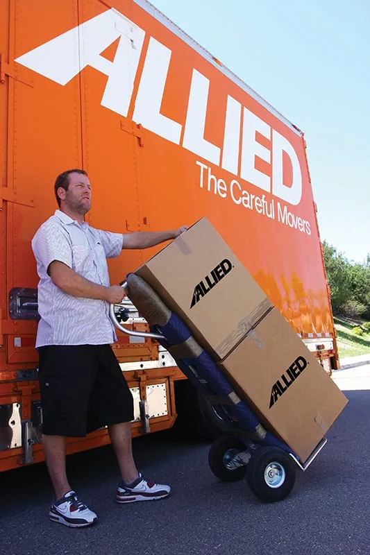 Mover rolling a dolly stacked with Allied moving boxes