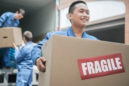 Two movers carrying a carton labeled fragile